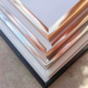 Pu&ograve; includere: Primo piano dell'angolo di quattro cornici con bordi metallici di diversi colori. Le cornici sono impilate l'una sull'altra, con la cornice superiore che ha un bordo dorato, la seconda cornice che ha un bordo argentato, la terza cornice che ha un bordo cromato e la cornice inferiore che ha un bordo nero.