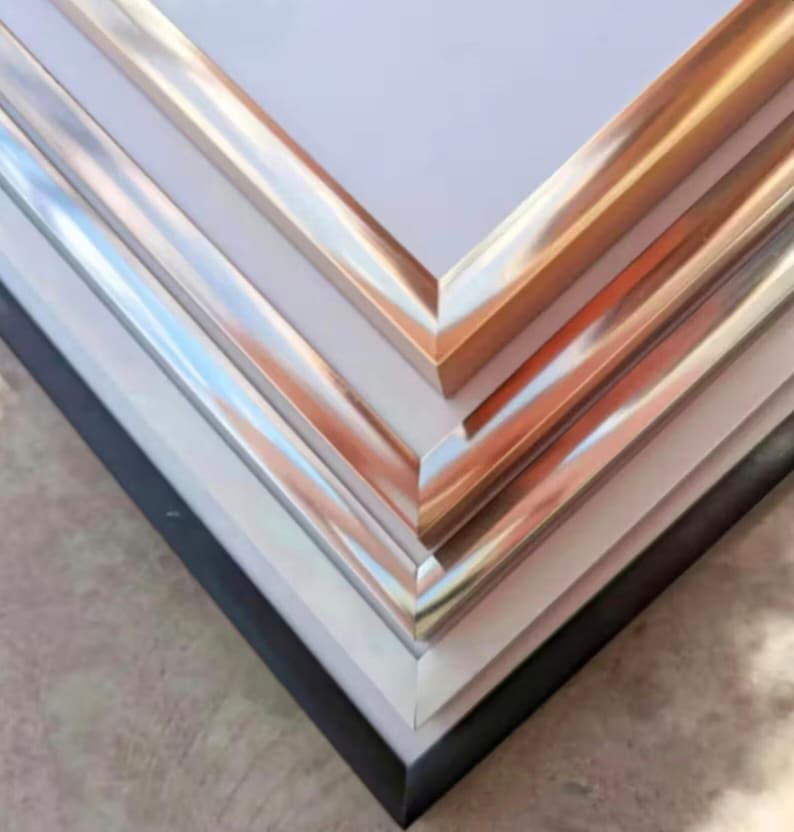 Pu&ograve; includere: Primo piano dell'angolo di quattro cornici con bordi metallici di diversi colori. Le cornici sono impilate l'una sull'altra, con la cornice superiore che ha un bordo dorato, la seconda cornice che ha un bordo argentato, la terza cornice che ha un bordo cromato e la cornice inferiore che ha un bordo nero.