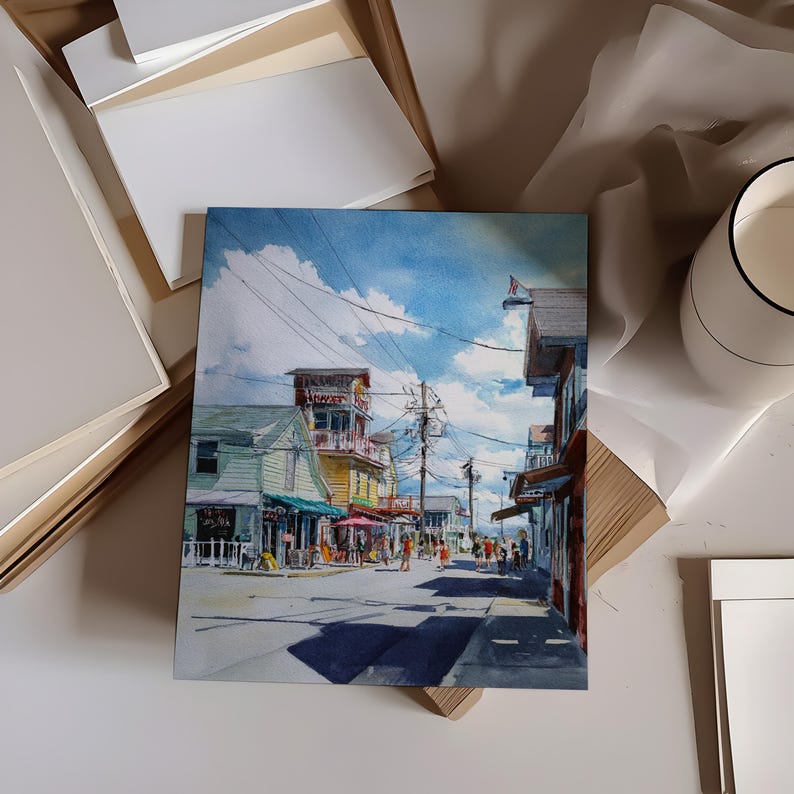May include: Watercolor painting of a street scene with shops and people. The buildings are painted in shades of green, yellow, and red, with awnings and a blue sky with clouds. The painting is on a white surface with other art supplies.