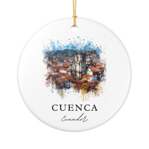 May include: A round white ceramic ornament featuring a watercolor-style illustration of the city of Cuenca, Ecuador, with its prominent cathedral and red-tiled roofs. The text CUENCA Ecuador is printed in black below the image, with a gold hanging cord.