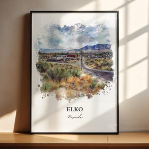 Op de afbeelding: Een aquarel schilderij van een klein stadje in Elko, Nevada. Het schilderij toont een weg die door het stadje slingert met gebouwen aan beide kanten. De lucht is lichtblauw met witte wolken. Het schilderij is ingelijst in een zwart frame.