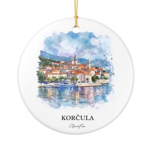 May include: A round ceramic ornament featuring a watercolor painting of Korčula, Croatia. The artwork depicts a coastal town with red-tiled roofs, a harbor, and the text "KORČULA Croatia" at the bottom. A gold string is attached for hanging.
