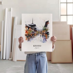 May include: A watercolor painting of a street scene in Kyoto, Japan. The painting features traditional Japanese architecture, including a pagoda, and people walking down the street. The painting is in a white frame and is being held by a person.