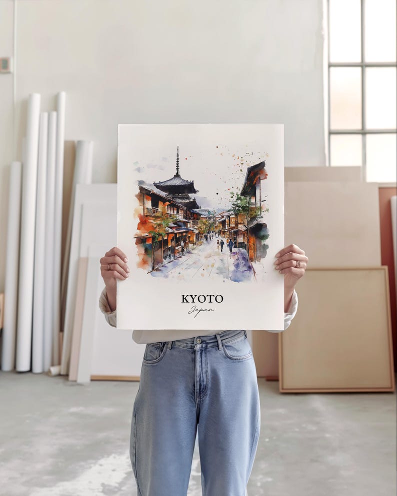 May include: A watercolor painting of a street scene in Kyoto, Japan. The painting features traditional Japanese architecture, including a pagoda, and people walking down the street. The painting is in a white frame and is being held by a person.