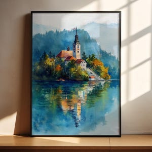 Può includere: Dipinto ad acquerello di una chiesa su un'isola in un lago. La chiesa ha un alto campanile e un tetto di tegole rosse. Alberi con fogliame autunnale circondano la chiesa. Il lago riflette la chiesa e il paesaggio. Il dipinto è in una cornice nera.