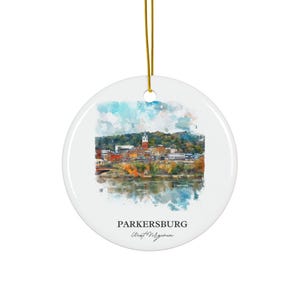Könnte beinhalten: Runder, weißer Keramik-Weihnachtsschmuck mit einem Aquarellgemälde von Parkersburg, West Virginia. Das Bild zeigt eine Stadtlandschaft mit einem Fluss und bunten Bäumen. Der Text "PARKERSBURG West Virginia" ist darunter gedruckt. Ein goldener Faden ist befestigt.