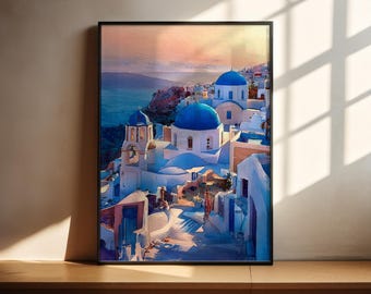 May include: Framed watercolor print of a coastal village with white buildings and blue domes. The artwork depicts a scenic view of a town with blue waters and a colorful sky. The print is in a black frame and is displayed on a wooden surface.