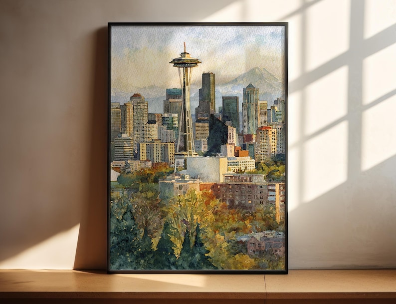 May include: Watercolor painting of the Seattle skyline, featuring the Space Needle and surrounding buildings. The artwork is framed in black and depicts a sunny day with a mountain in the background. The painting has a warm color palette.