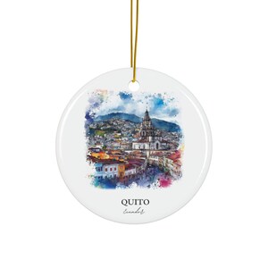 May include: A white ceramic bauble featuring a watercolour painting of Quito, Ecuador. The painting depicts a cityscape with a church at its centre. The text "QUITO Ecuador" is written beneath the painting.