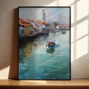 Könnte beinhalten: Gerahmtes Aquarellgemälde einer Uferlandschaft mit farbenfrohen Gebäuden, einem hohen weißen Turm und Booten auf dem Wasser. Das Gemälde hat einen schwarzen Rahmen und wird auf einer Holzoberfläche ausgestellt.