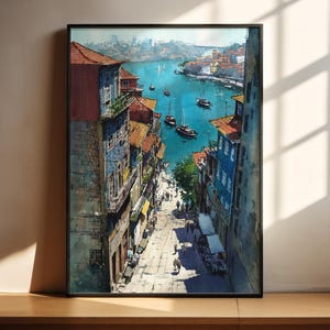 Puede incluir: Una pintura de acuarela enmarcada representa un paisaje urbano europeo con edificios en tonos azules, rojos y amarillos. La obra de arte muestra una escena frente al mar con barcos en el agua y personas caminando por una calle adoquinada. La pintura se exhibe sobre una superficie de madera.