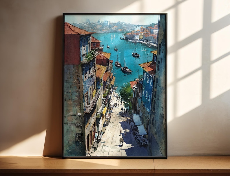 Puede incluir: Una pintura de acuarela enmarcada representa un paisaje urbano europeo con edificios en tonos azules, rojos y amarillos. La obra de arte muestra una escena frente al mar con barcos en el agua y personas caminando por una calle adoquinada. La pintura se exhibe sobre una superficie de madera.