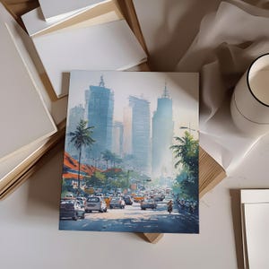 May include: A watercolor print of a city street scene with tall buildings, palm trees, and traffic. The artwork features a soft color palette of blues, oranges, and greens, with a focus on the urban landscape. The print is displayed on a white surface.