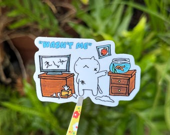 May include: A white cat with a black X on its forehead stands in front of a broken television and a fishbowl. The cat is pointing at the fishbowl with its right paw. The text "Wasn't me" is written above the cat.