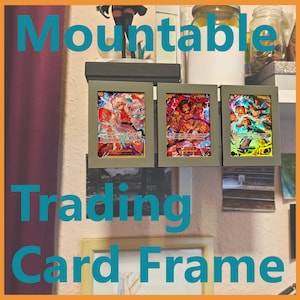 Könnte beinhalten: Drei graue, montierbare Sammelkartenrahmen, die jeweils eine farbenfrohe Karte enthalten. Die Rahmen sind an einer Wand montiert, mit dem Text "Mountable Trading Card Frame" in Türkis. Die Karten zeigen lebendige Illustrationen.