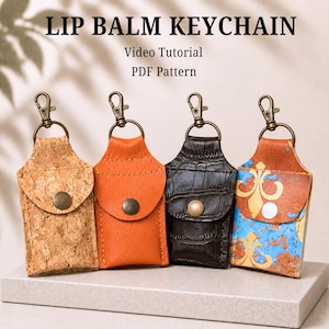 Könnte beinhalten: Vier Lippenbalsam-Schlüsselanhänger mit Metallkarabinern und Druckknöpfen. Die Etuis haben verschiedene Texturen: Naturkork, einfarbiges Orange, schwarze Krokodilprägung und Blau mit goldenen Lilienmustern. Text: LIP BALM KEYCHAIN Video Tutorial PDF Pattern.