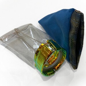 Op de afbeelding: Een gouden en groene iriserende horlogeband met een transparante plastic behuizing en een blauwe fluwelen tas.
