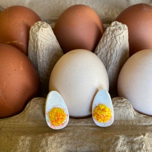 May include: Two white eggs with yellow yolks are in a cardboard egg carton with brown eggs. The eggs are decorated with white and yellow glitter.