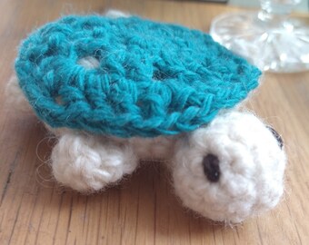 May include: A crocheted turtle toy with a teal shell and white body. The turtle has black eyes and is made with soft yarn.