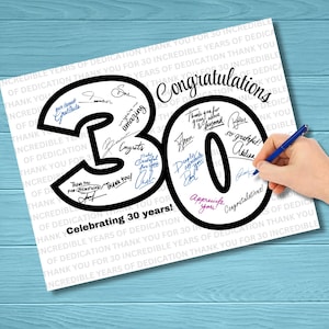 Könnte beinhalten: Eine weiße Karte mit einer großen schwarzen "30" und "0" Form, gefüllt mit Unterschriften und den Worten "Glückwunsch" und "Feiert 30 Jahre!". Eine Hand mit einem blauen Stift unterschreibt die Karte. Der Hintergrund ist ein blaues Holzmaserung.