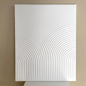 Pode incluir: Arte de parede de tela branca com um design texturizado em relevo de semicírculos concêntricos sobrepostos.