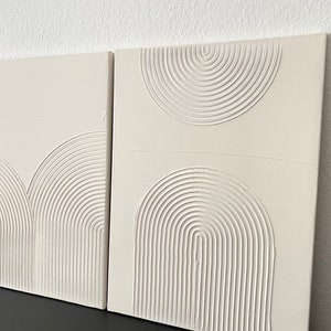 May include: Two white canvas paintings with raised, textured, concentric circles in a geometric pattern.