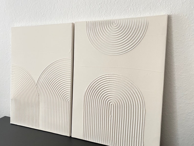 May include: Two white canvas paintings with raised, textured, concentric circles in a geometric pattern.