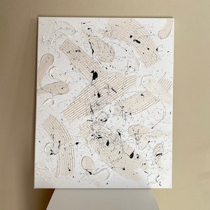 以下が含まれることがあります： 白と黒の絵の具で描かれたキャンバス上の抽象画。絵画は、円、正方形、縞模様など、さまざまな形と線を特徴としています。