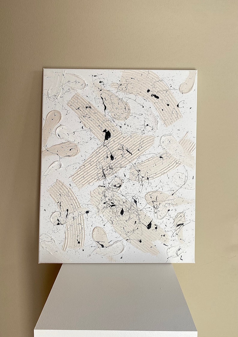 以下が含まれることがあります： 白と黒の絵の具で描かれたキャンバス上の抽象画。絵画は、円、正方形、縞模様など、さまざまな形と線を特徴としています。