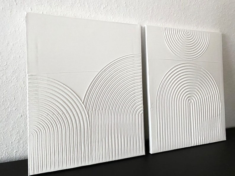 May include: Two white canvas wall art pieces with raised, textured, concentric circles in a geometric pattern.
