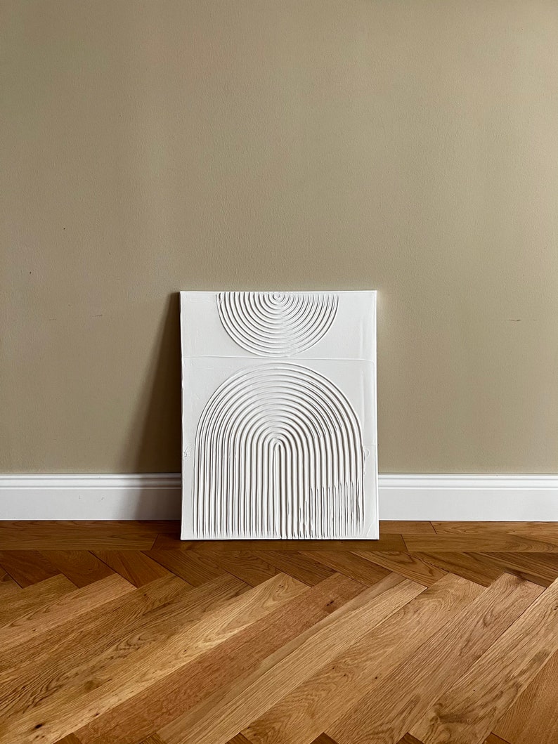 May include: White abstract wall art with a raised design of overlapping circles and arches. The art is on a beige wall with a wood floor.