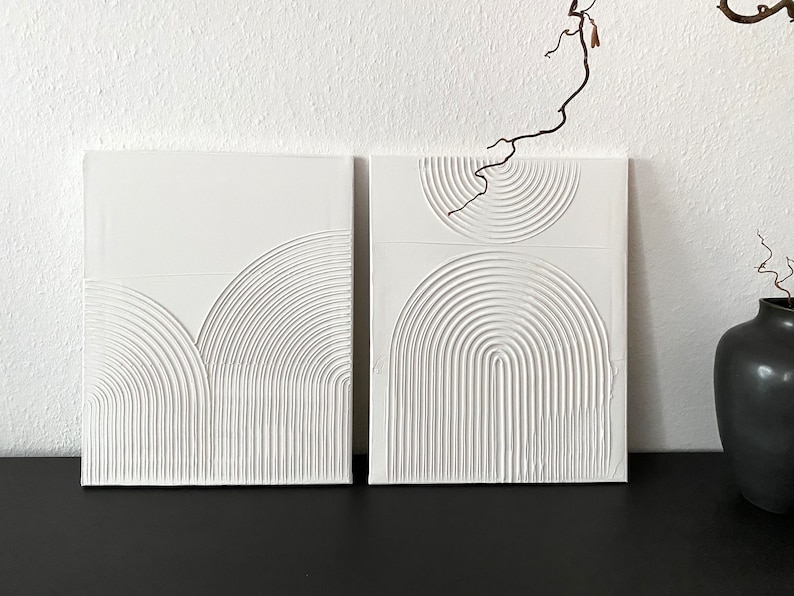 May include: Two white square canvases with raised, embossed, concentric circles and semi-circles in a geometric pattern.