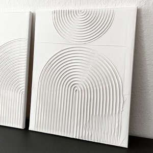 May include: Two white canvas paintings with raised, textured, concentric circles in the shape of half-circles.