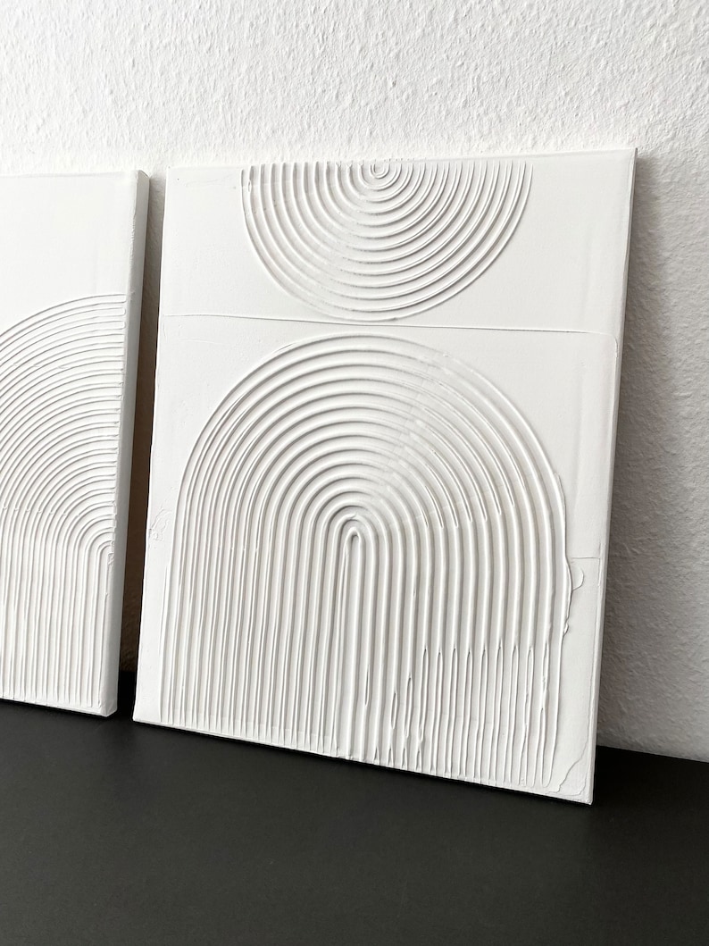 May include: Two white canvas paintings with raised, textured, concentric circles in the shape of half-circles.