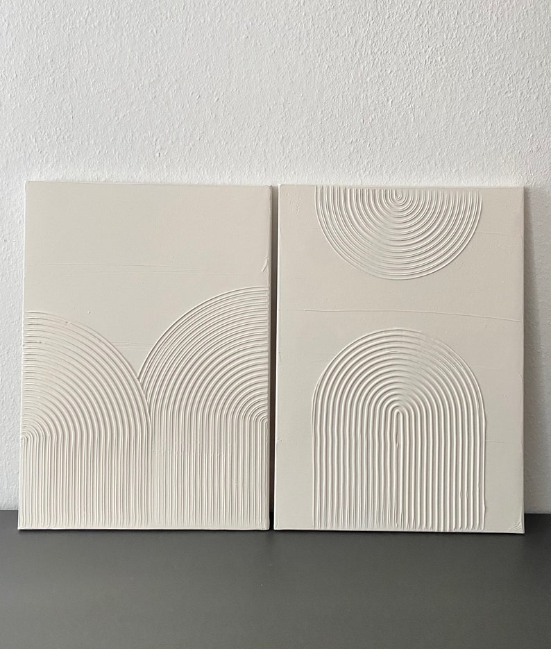 May include: Two white canvas panels with raised, textured, geometric designs. The designs are made of concentric circles and arcs, creating a modern and minimalist aesthetic.