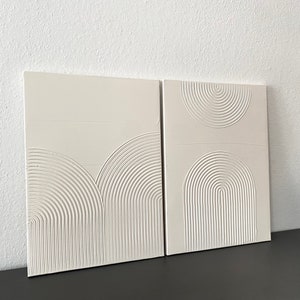 May include: Two white canvas panels with raised, embossed, concentric circles in a semi-circular pattern. The panels are displayed on a black surface.