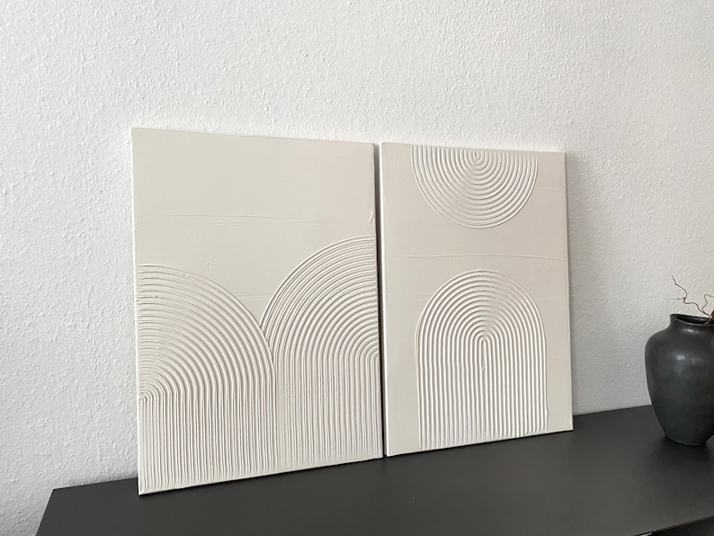 May include: Two white canvas panels with raised, embossed, concentric circles in a semi-circular pattern. The panels are displayed on a black surface.