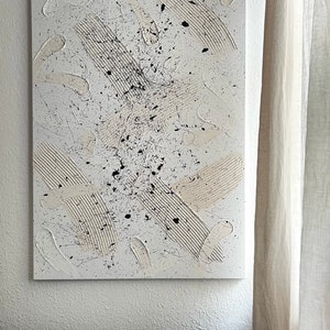 以下が含まれることがあります： 白、黒、ベージュの塗料を使用したキャンバス上の抽象画。絵画はテクスチャのある表面を持ち、さまざまな筆跡と飛沫を特徴としています。