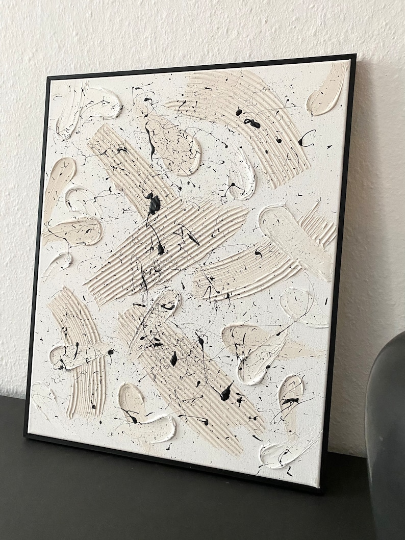 以下が含まれることがあります： 白のキャンバスに黒と白の塗料で描かれた抽象画。塗料は、はね、線、渦巻きなど、さまざまなテクスチャで塗られています。
