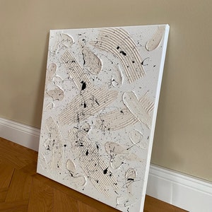 以下が含まれることがあります： 白と黒の塗料でキャンバスに描かれた抽象画。絵画はテクスチャのある表面を持ち、さまざまな形と線を特徴としています。