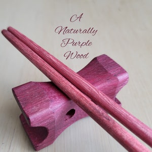 May include: A pair of purple wooden chopsticks resting on a purple wooden chopstick holder. The text "A Naturally Purple Wood" is written above the chopsticks.