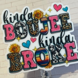 May include: A white background with a pink, black, and brown graphic that reads "kinda boujee kinda broke". The graphic is decorated with sunflowers, hearts, and leopard print. The graphic is attached to a clear retractable badge holder.
