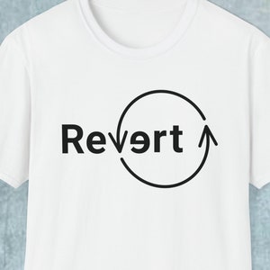 Puede incluir: Camiseta blanca con un círculo negro y una flecha gráfica y el texto "Revert" impreso en la parte delantera.