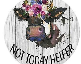 May include: A watercolor illustration of a cow with a floral crown on a white wood background. The cow is looking at the viewer and the text "Not Today Heifer" is written below the cow.