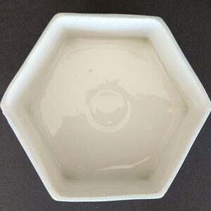 May include: White ceramic hexagonal dish with a smooth, glossy finish. The dish is empty and has a slight curve to the sides.