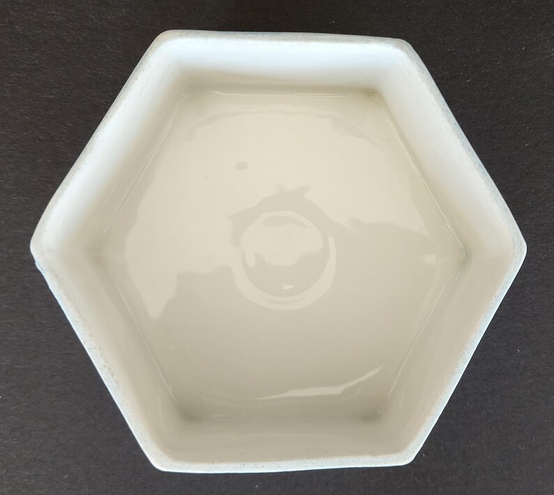 May include: White ceramic hexagonal dish with a smooth, glossy finish. The dish is empty and has a slight curve to the sides.