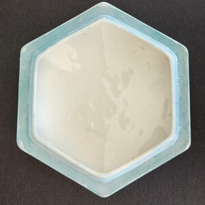 May include: A light blue hexagonal ceramic lid with a white interior. The lid has a smooth, glossy finish.