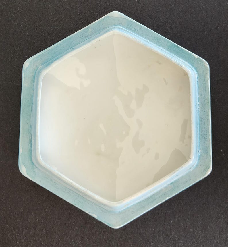May include: A light blue hexagonal ceramic lid with a white interior. The lid has a smooth, glossy finish.