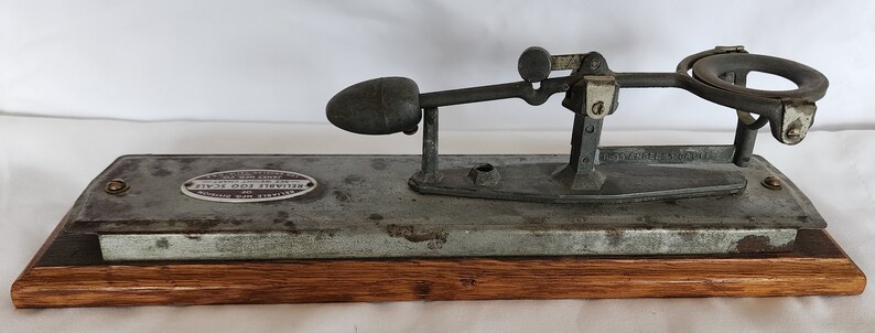 Peut inclure: Un testeur d'&oelig;ufs vintage en m&eacute;tal avec une base en bois. Le testeur a un bras en m&eacute;tal avec un porte-&oelig;uf lest&eacute; et une &eacute;chelle pour mesurer la fra&icirc;cheur de l'&oelig;uf.