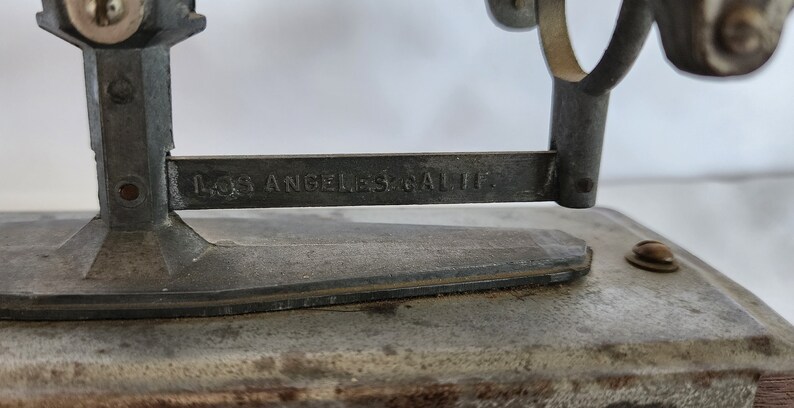 Peut inclure: Une balance en m&eacute;tal vintage avec une finition argent&eacute;e. La balance a une base en m&eacute;tal et un bras en m&eacute;tal avec l'inscription "Los Angeles, Calif."